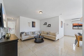 A modern living room with a sofa, coffee table, and a dining area with chairs. - Felicidad: Stunning 3BR Retreat with Private Pool (Oranjestad)