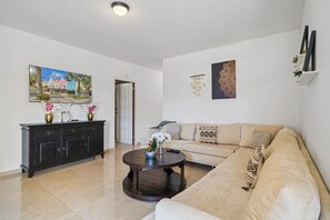 Una sala de estar con un sofá, una mesa de centro y un armario. Hay un cuadro en la pared y una puerta que da a otra habitación.