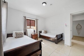 A hotel room with two beds, a nightstand, a lamp, and a window with curtains. - Felicidad: Stunning 3BR Retreat with Private Pool (Oranjestad)