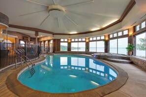 A large indoor swimming pool with a view of the outdoors, a ceiling fan, and a staircase leading to an upper level.