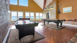 Tilava huone, jossa on biljardipöytä, pöytäjalkapallopöytä ja suuret ikkunat, joista avautuu näkymä vesistöön.