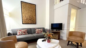 A living room with a grey sofa, two floral cushions, a coffee table with a vase, and two leather armchairs. A flat-screen TV is on a stand to the right. - L'appartement Pierre Charron C (Paris)