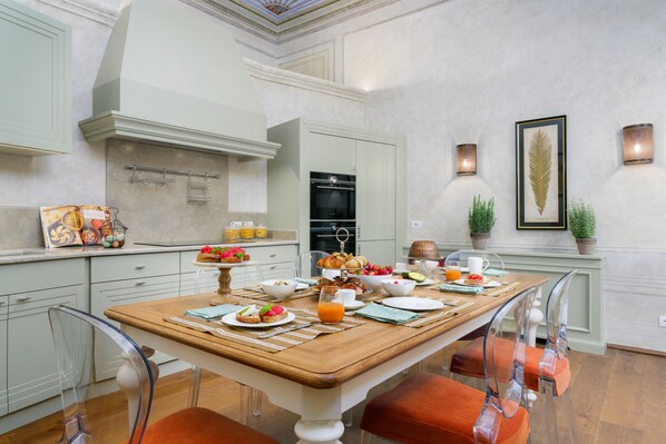 Un comedor con una mesa de madera dispuesta para el desayuno, rodeada de sillas transparentes.