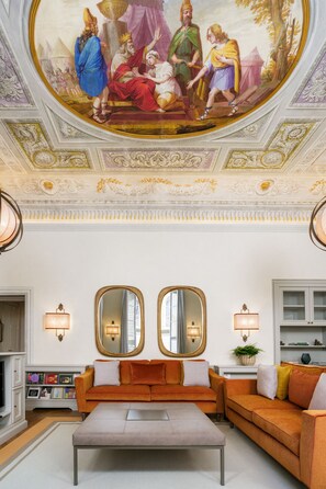 Una habitación lujosa con un fresco clásico, muebles elegantes y detalles ornamentales en el techo.
