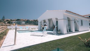 En moderne villa med swimmingpool, udendørs møbler og udsigt over det omkringliggende landskab.