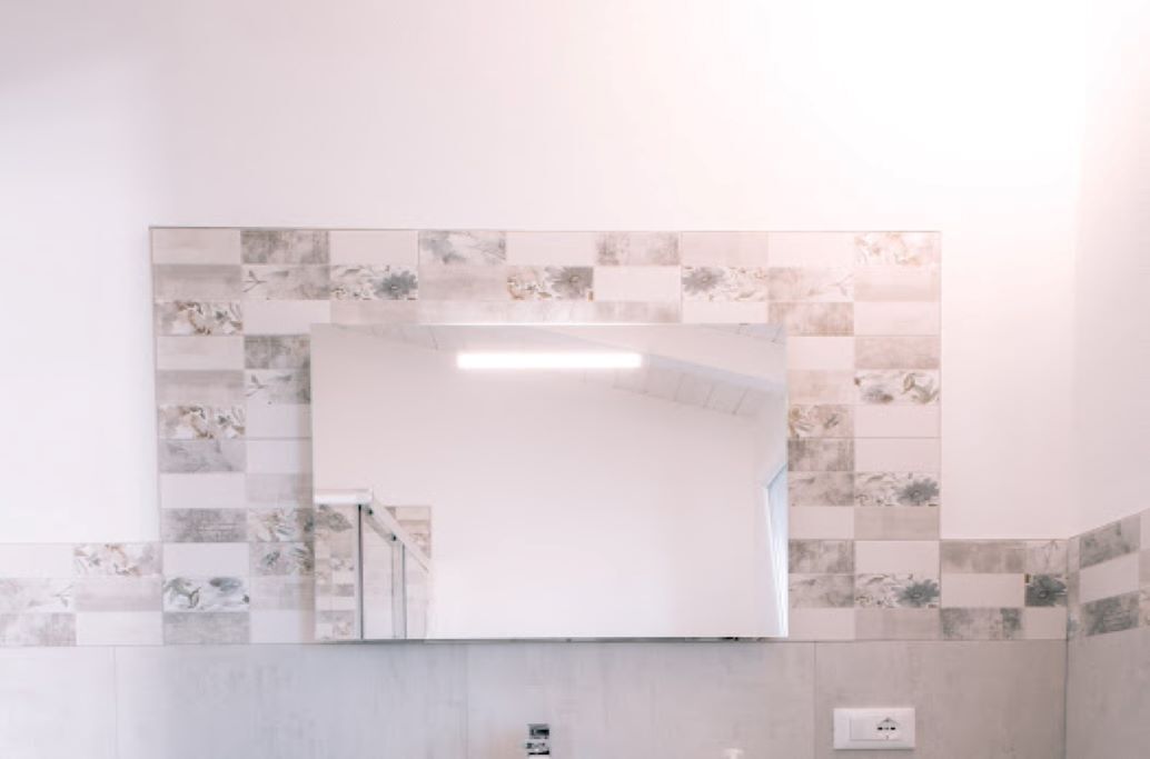 A bathroom with a large mirror, tiled walls, and a light switch on the wall.