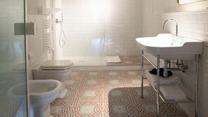A bathroom with a patterned floor, a white sink, and a glass shower enclosure. - Luxury Apartment with view on Piazza Pitti (Firenze)