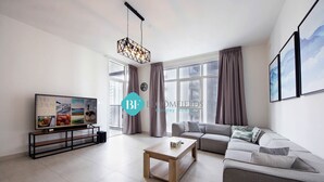Ein modernes Wohnzimmer mit einer Couch, einem Couchtisch, einem Fernseher auf einem Schrank und einem großen Fenster mit Vorhängen.