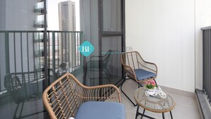 Ein Balkon mit Korbstühlen und einem Glastisch, Blick auf eine Stadtlandschaft, und ein Logo für "Holiday Homes".