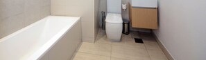 Een moderne badkamer met een badkuip, toilet en een prullenbak.