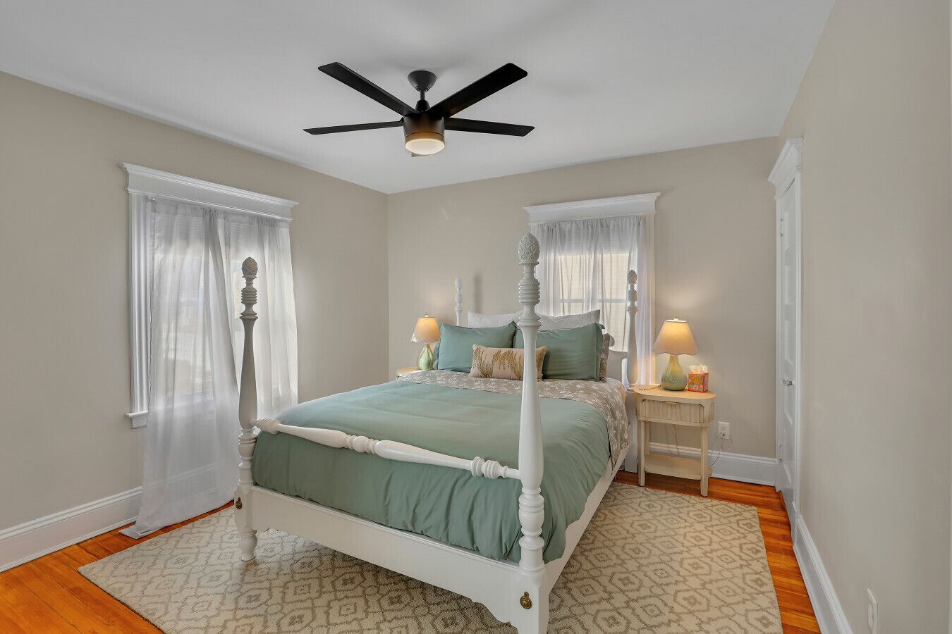 Une chambre à coucher avec un lit à baldaquin, un ventilateur de plafond, deux tables de chevet avec des lampes et un tapis à motifs.