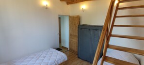 Une petite pièce compacte avec deux lits simples, une échelle en bois, une armoire et une porte donnant sur une autre pièce.
