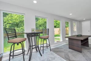 Una cocina con dos taburetes de bar, una mesa central y ventanas amplias que dan a un jardín.