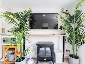 Enjoy a cozy living space with a large flat-screen TV, wood-burning stove, and lush greenery.
