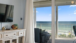 Una habitación con televisión, cómoda y vista al océano a través de una puerta corrediza de vidrio.