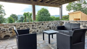 Un patio al aire libre con suelo de piedra, mobiliario de mimbre y una pared de piedra.