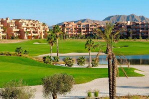 A golf course with sand bunkers, palm trees, and a body of water.