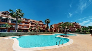 A swimming pool area with multiple pools, palm trees, and a building with balconies.