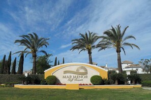 A sign for Mar Menor Golf Resort with palm trees and a clear sky.