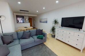 A modern living room with a grey sofa, a flat-screen TV on a white cabinet, a dining area with a table and chairs, and a potted plant. - Spacious ground floor apartment - EO2402MM (Mar Menor Golf Resort)