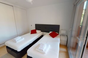 A hotel room with two beds, each with a pillow and a rolled towel. There is a bedside table with a lamp, a wardrobe, and a sliding glass door leading to an outdoor area. - Spacious ground floor apartment - EO2402MM (Mar Menor Golf Resort)