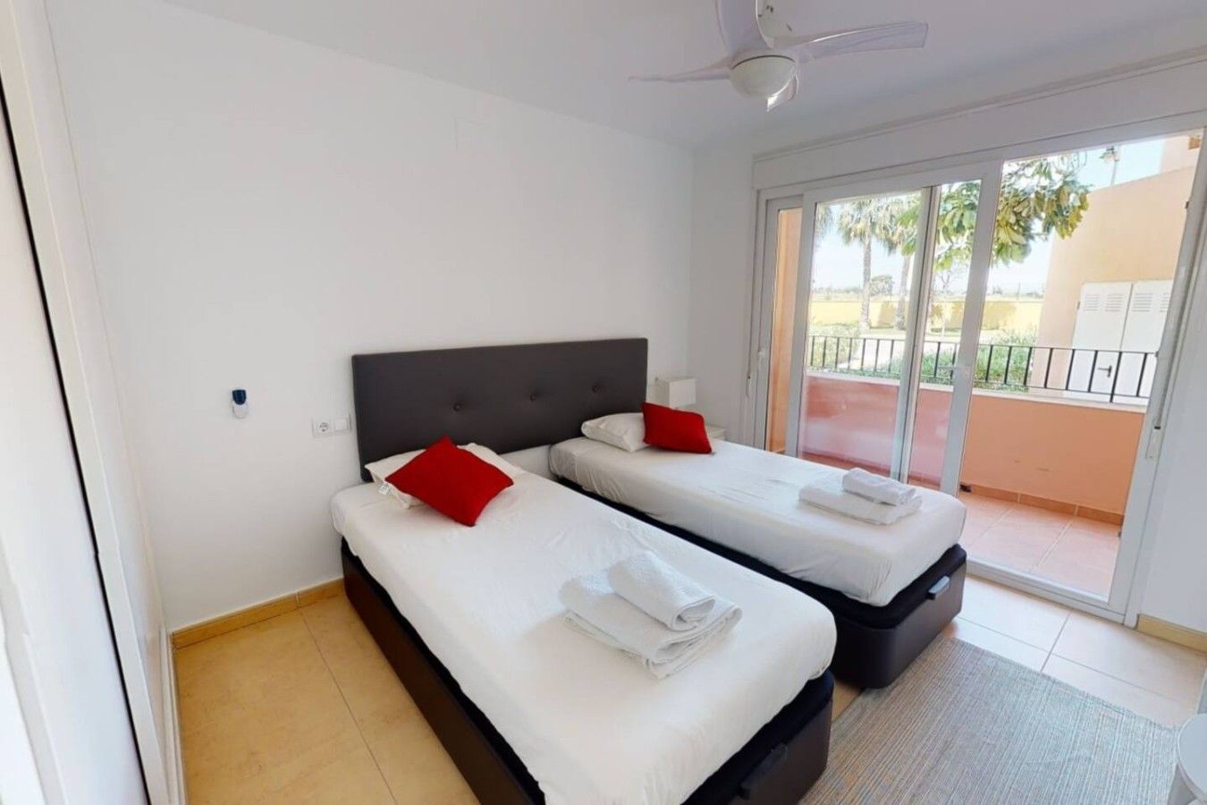 Ein Hotelzimmer mit zwei Betten, einem Deckenventilator und einer Schiebetür zu einem Balkon.