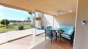 A balcony with a sofa, a table, and chairs, offering a view of a landscaped area.