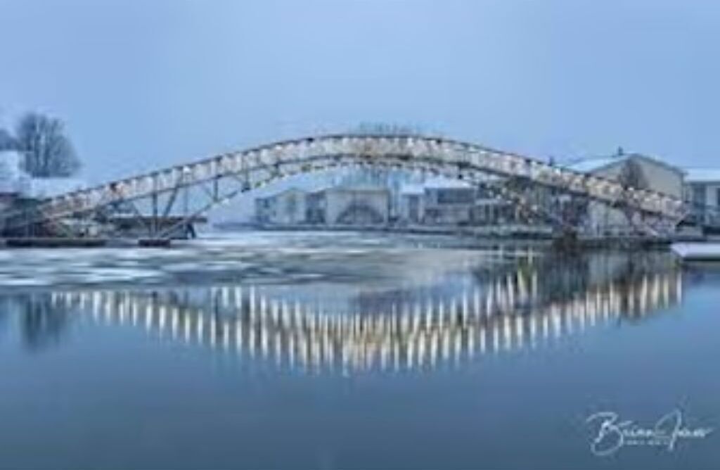 Un puente sobre una masa de agua congelada, con el reflejo del puente y edificios en el hielo.