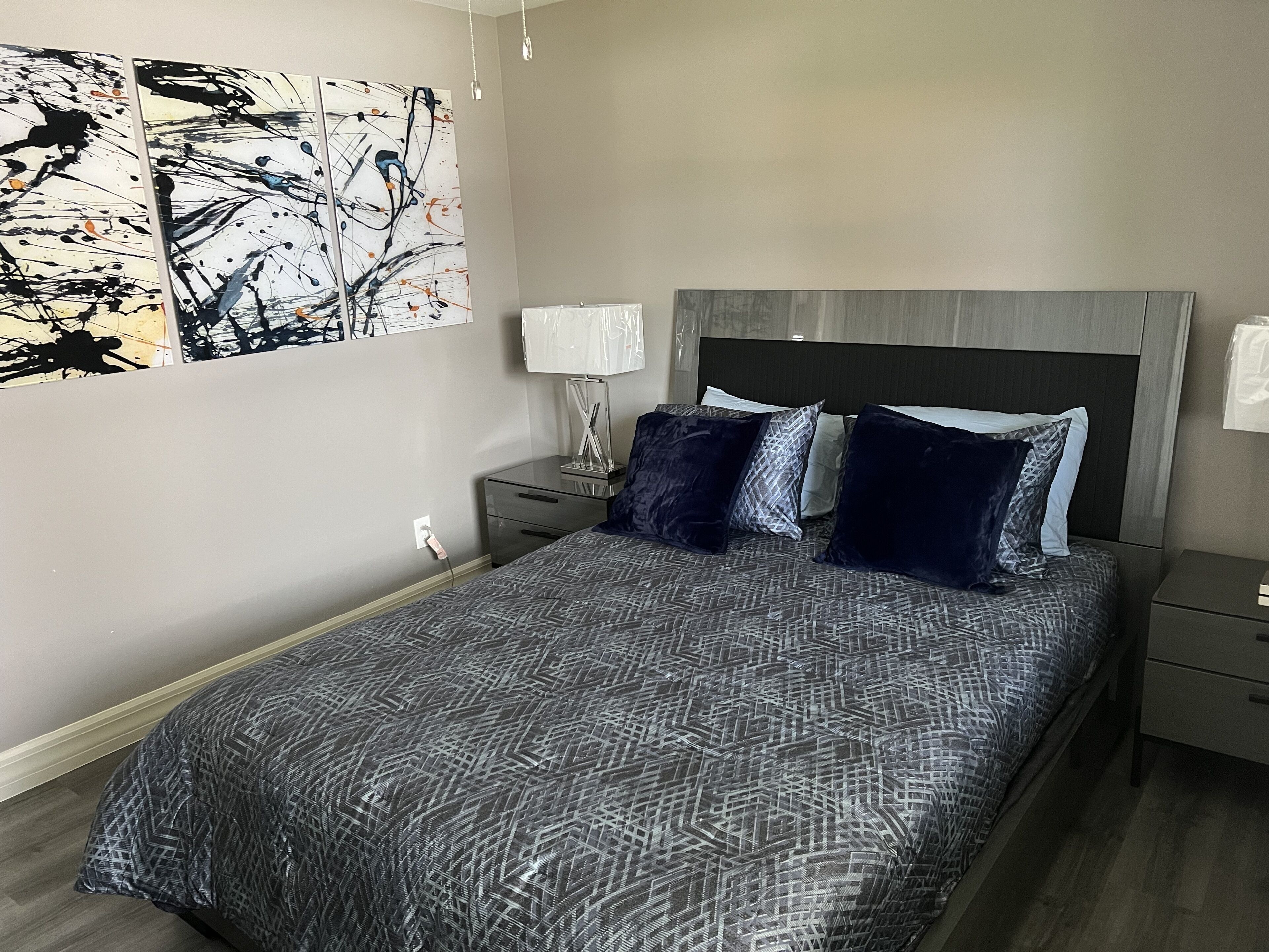 Een slaapkamer met een bed, nachtkastjes, een lamp en abstracte decoratie aan de muur.