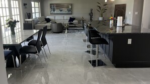 A modern kitchen with a marble countertop, black bar stools, and a dining area with black chairs. -  Luxury Waterfront Retreat, 5thAve,  Private Pool, Dock & Sunset View Naples Bay (Naples)