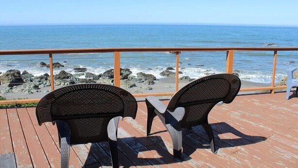 A wooden deck with two black chairs facing the ocean. - Ocean Front Cabin 16 with Private Jacuzzi & Incredible Views (Private Beach by White Rock Resort) (Smith River)