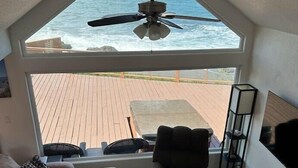 A cozy living room with a large window overlooking the ocean, a ceiling fan, and a wooden coffee table. - Ocean Front Cabin 16 with Private Jacuzzi & Incredible Views (Private Beach by White Rock Resort) (Smith River)