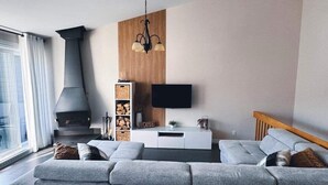 A modern living room with a grey sofa, a fireplace, a TV mounted on the wall, and a wooden accent wall. - Le Bionick- Condo à louer Stoneham  (Stoneham-et-Tewkesbury)