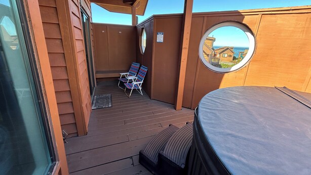 Een houten terras met een jacuzzi, twee ligstoelen en uitzicht op een gebouw met een balkon.