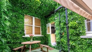 A garden area with a wooden table and benches, surrounded by lush greenery and a window. - Chic Studio in the ♥️ of Marylebone ❄️ Air Con. 🌿 Private Patio | Sleeps 3 (Greater London)