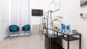 A modern room with a black desk, two blue chairs, a radiator, a Netflix sign, a mirror, and a shelf with water bottles and a clock. - Trastevere Suites - Top Collection (Rome)