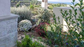 A garden with a variety of plants and flowers, a stone structure, and a view of a hilly landscape.
