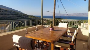 A wooden table with chairs on a balcony overlooking a coastal landscape.