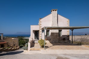 Una casa moderna con fachada de piedra, un porche cubierto y vista al mar.