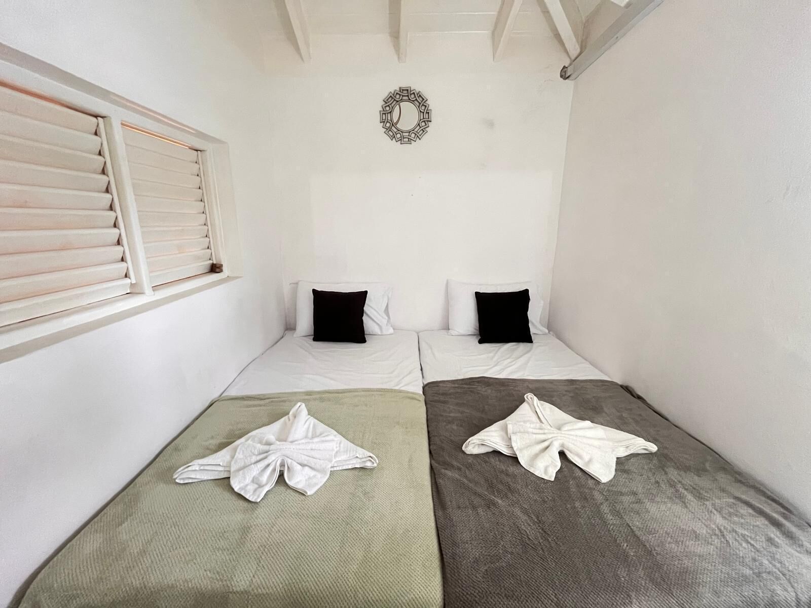 A small, clean room with two single beds, a window with blinds, and a decorative wall piece.