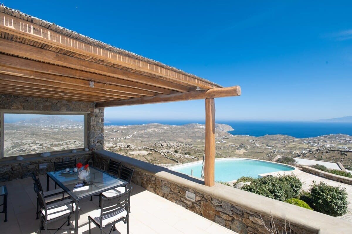 Une terrasse avec une table et des chaises, donnant sur un paysage côtier et une piscine.