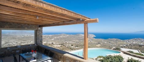 Une terrasse avec une table et des chaises, donnant sur un paysage côtier et une piscine.