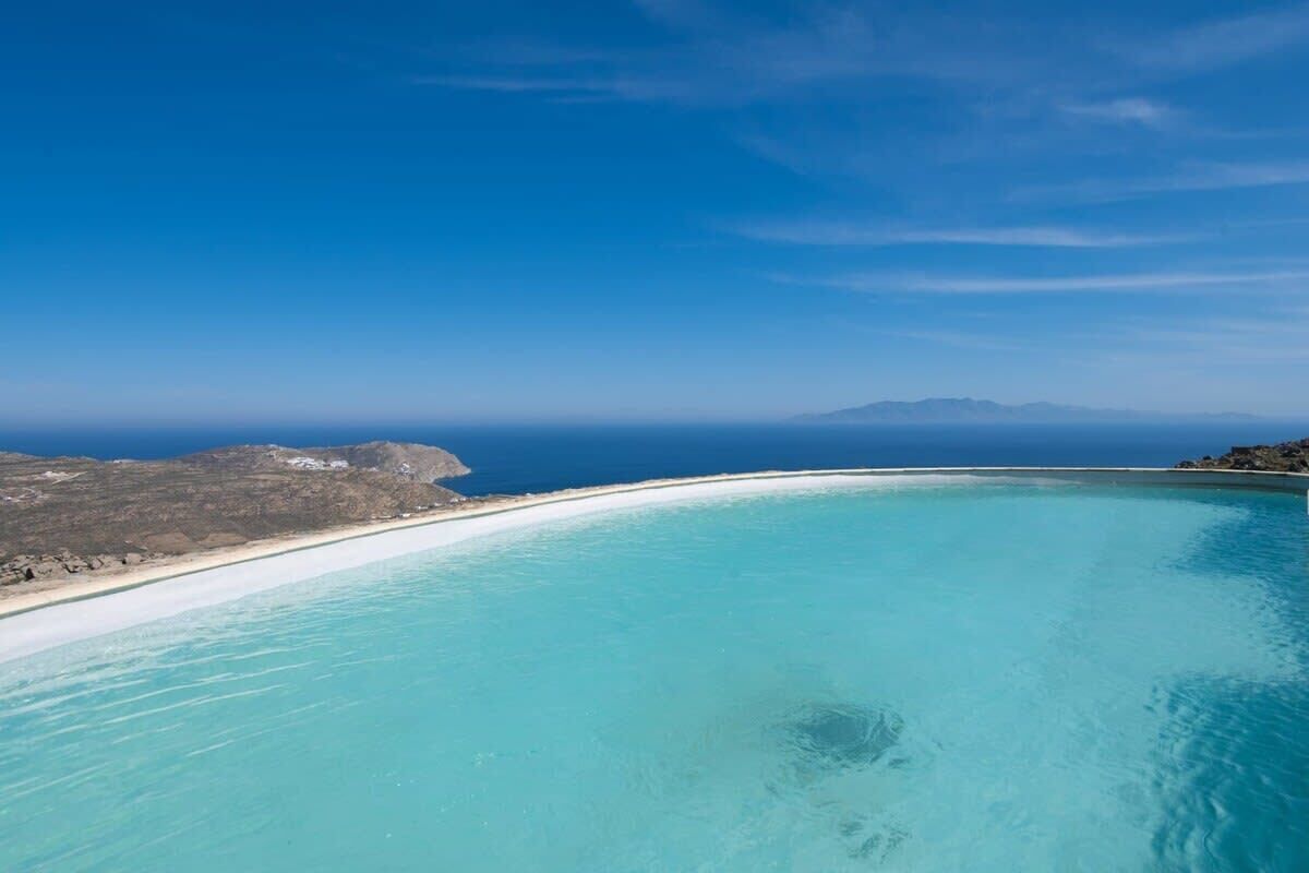 Un paisaje costero con cielo azul despejado, una playa arenosa y un mar turquesa tranquilo.