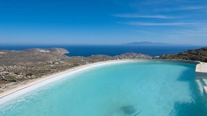 Un cielo azul despejado, una piscina curvada y una playa con terreno rocoso.