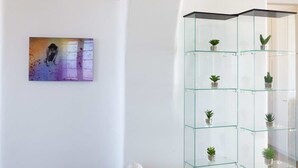 Una sala de estar con un sofá, un aparador de vidrio con plantas y un cuadro en la pared.