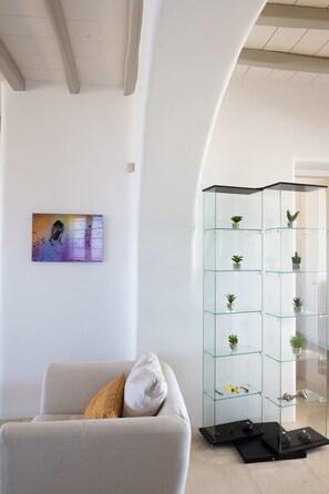 A living room with a sofa, a glass display unit with plants, and a painting on the wall.