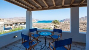 A covered outdoor seating area with a table and chairs, overlooking a coastal landscape with a clear view of the sea and distant hills. - Villa Victoria with Sea View and Two Private Pools (Mykonos)