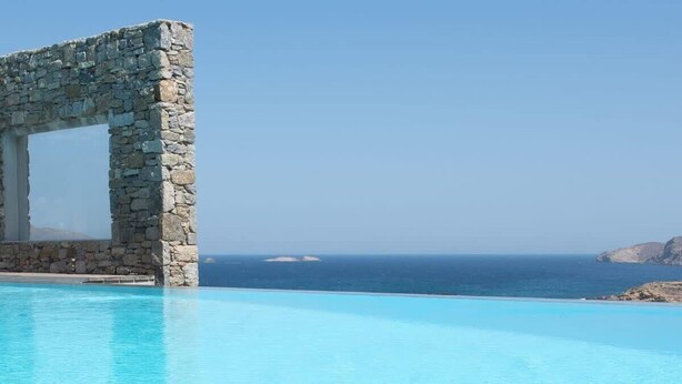 A stone arch structure over a clear blue pool with a view of the sea and distant land. - Villa Victoria with Sea View and Two Private Pools (Mykonos)