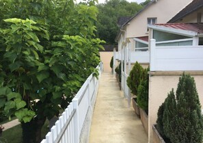 Uma trilha estreita ladeada por uma cerca branca e uma fileira de casas com fachada bege e telhados vermelhos.