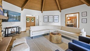 A modern living room with a white sectional sofa, a round wicker coffee table, and a wooden ceiling.
